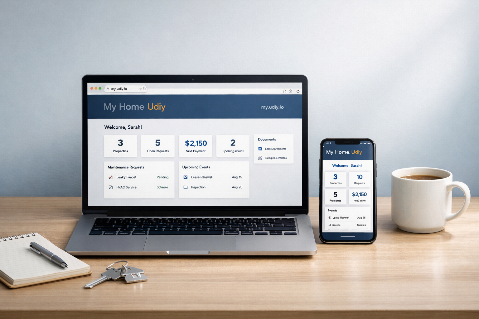 Editorial hero image of laptop and smartphone showing the My Home Udiy dashboard with house key and notebook on a clean desk.